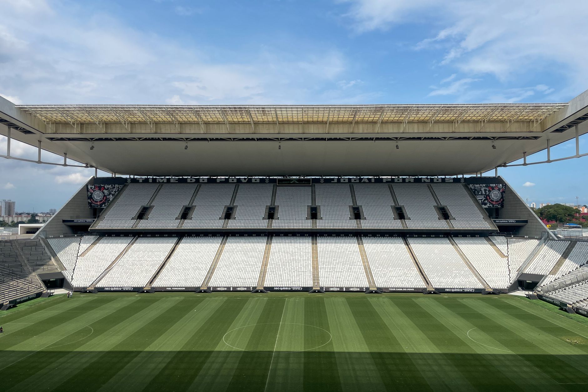 Wide view of an empty football arena in São Paulo, featuring a green pitch under a sunny sky.